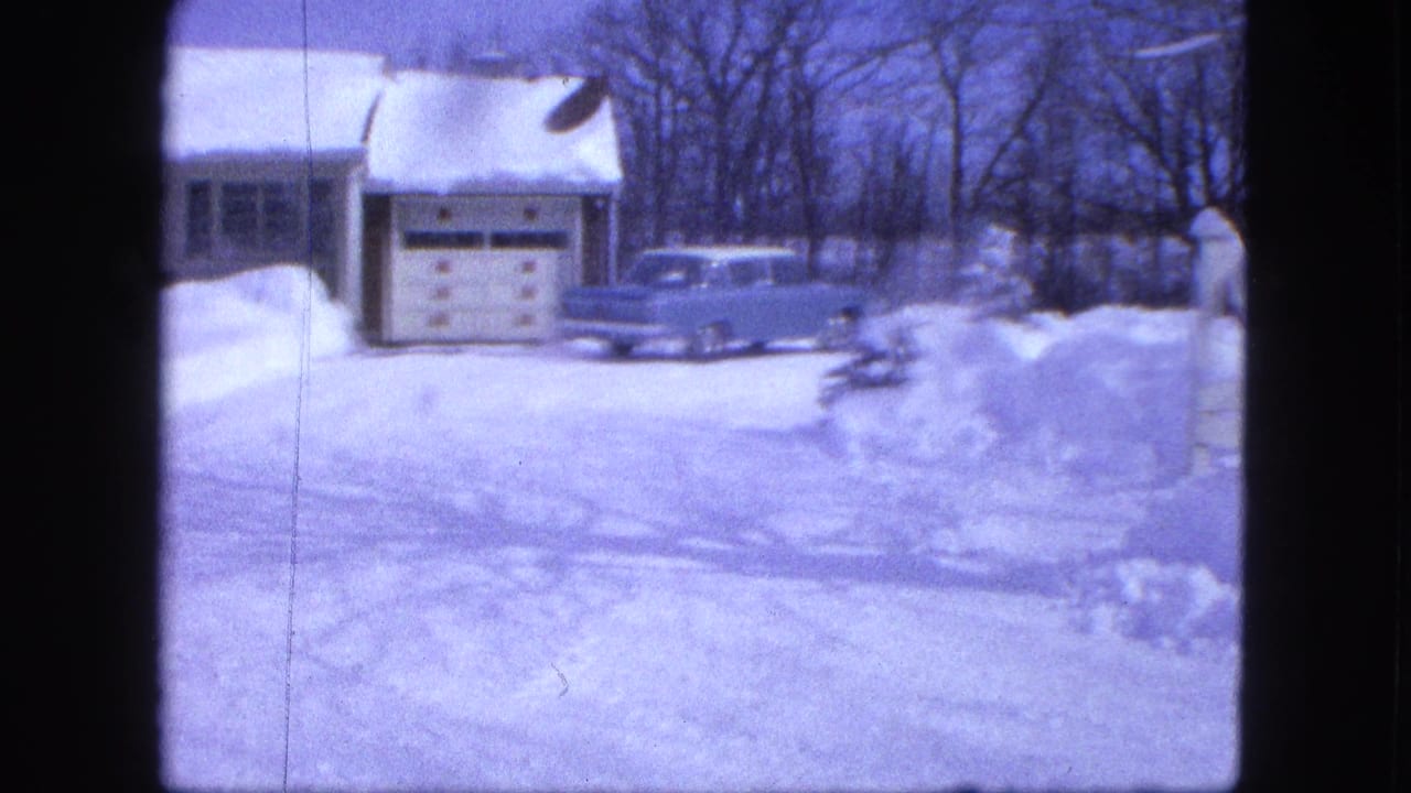 Snow-covered house and garage with a light blue car parked outside.