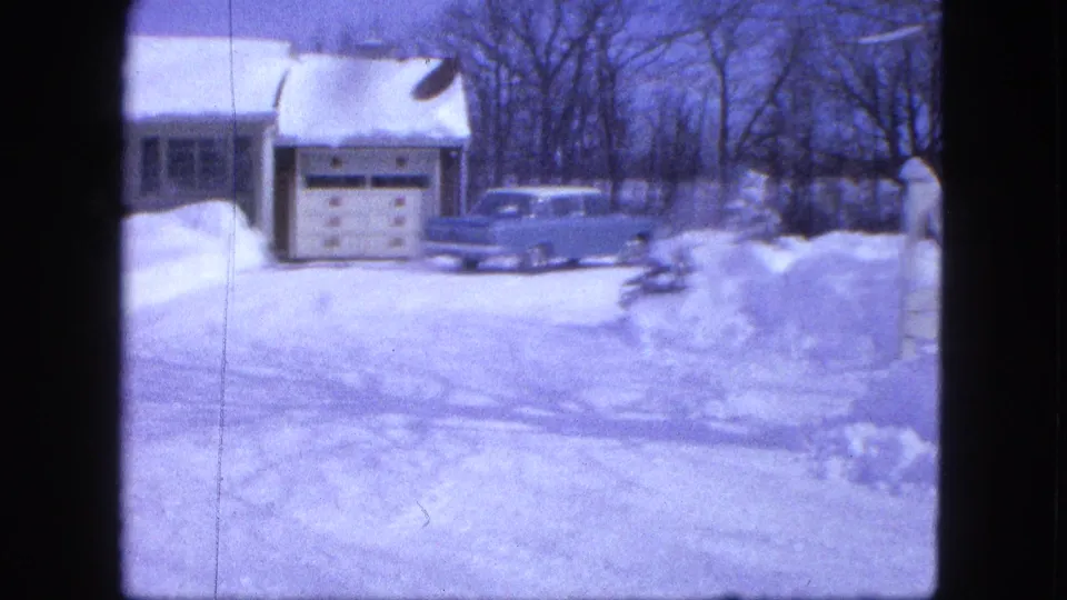 1963 Proctor, Minnesota home-movie frame showing a snow-covered house, garage, and light blue mid-century car.