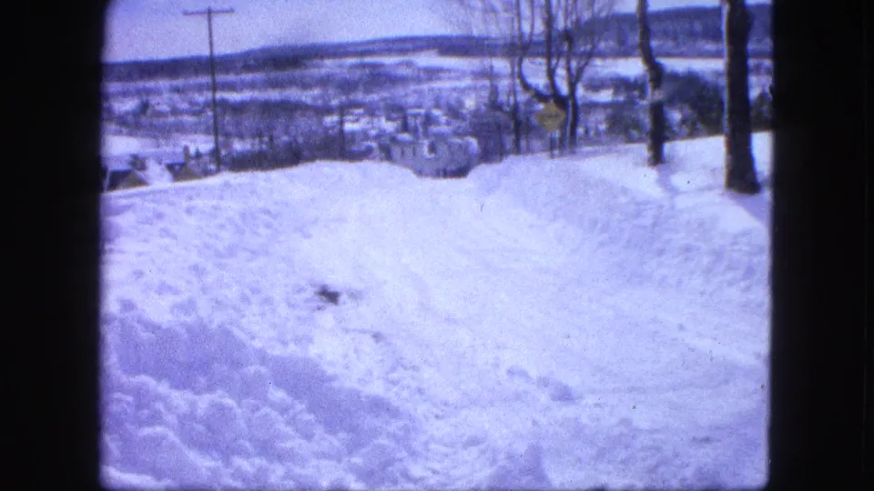 1963 winter home-movie view from a snowy hillside in Proctor, Minnesota, looking toward town buildings below.