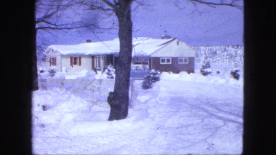 1963 Proctor, Minnesota 8mm frame showing a snowy house and yard, with a large bare tree trunk in front.