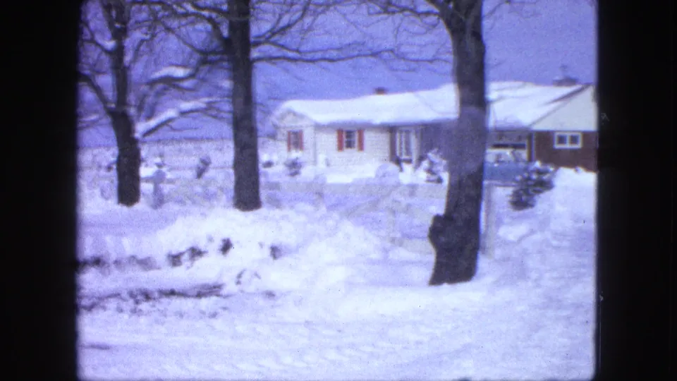 1963 Proctor, Minnesota home-movie frame showing a snow-covered single-story house behind bare trees and heavy yard snow.