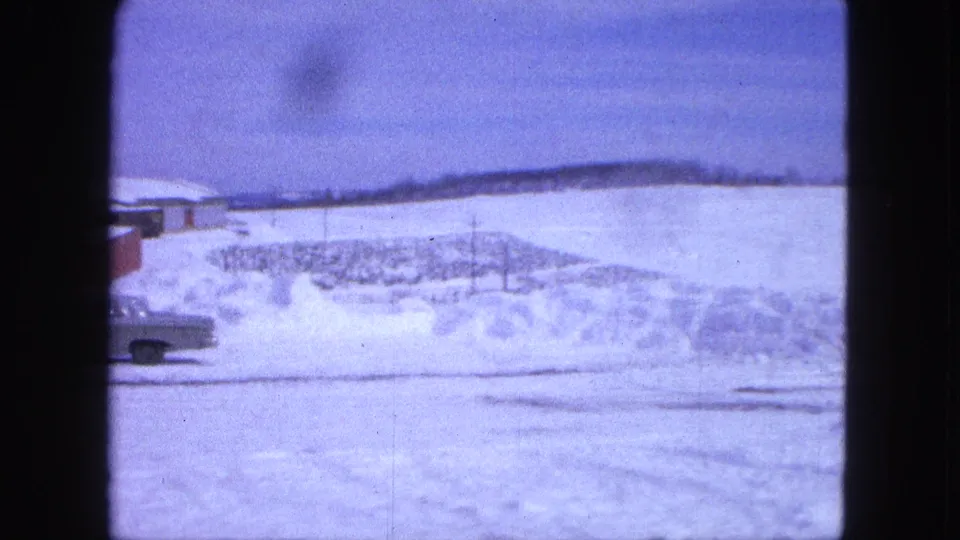 1963 Proctor, Minnesota roadside view with deep snow, a partial classic car, red building edge, and distant low hills.