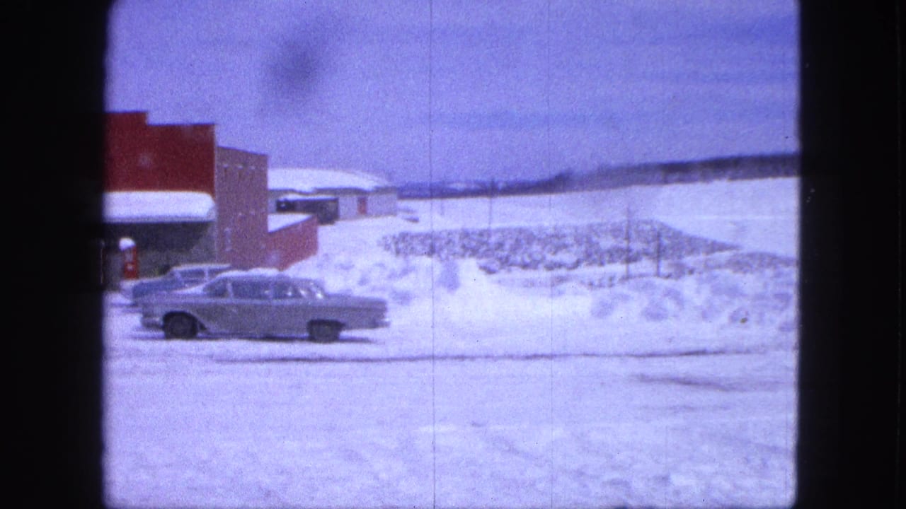 Silver sedan parked or moving near a red building with heavy snowbanks behind it.