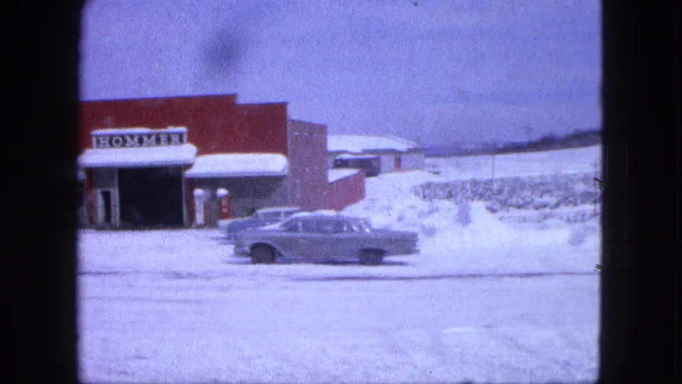 Red commercial building with partial HOMMER sign and classic sedan in a snowy Proctor, Minnesota parking area.