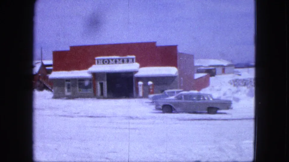 1963 Proctor, Minnesota frame showing the HOMMER-signed red building, classic sedan, snowbanks, and road surface.