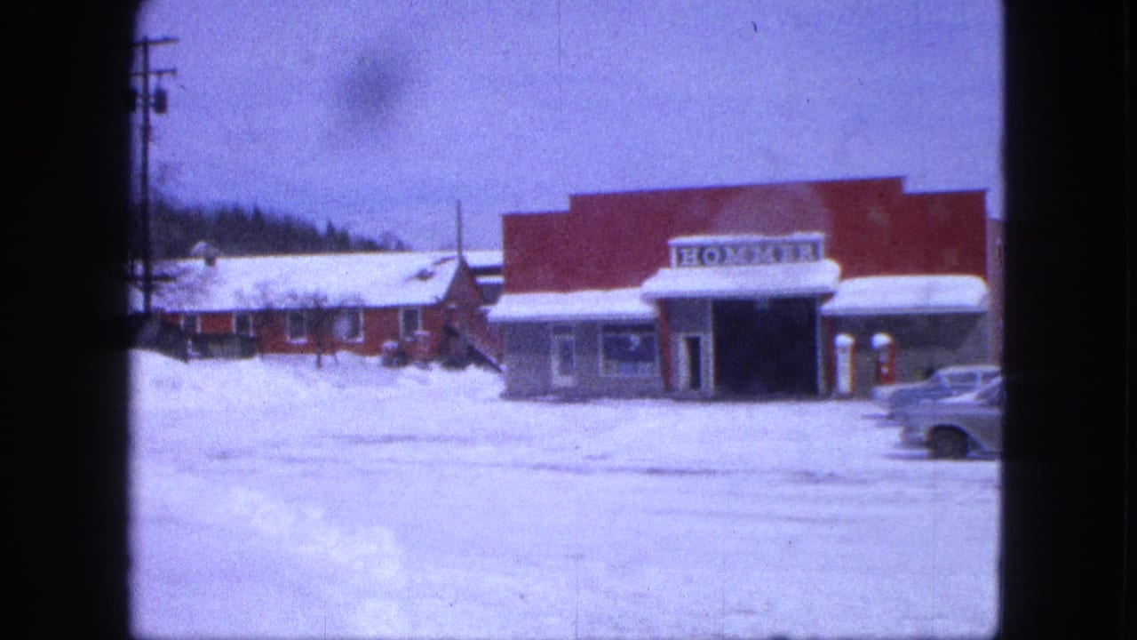 Snowy 1963 Proctor street view with a red HOMMER storefront, deep snowbanks, utility poles, and part of a car entering the frame.