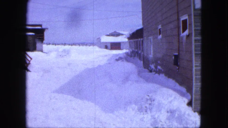 1963 Proctor, Minnesota view down a snowbound side lane beside wood-sided buildings, with a small outbuilding beyond the drifts.
