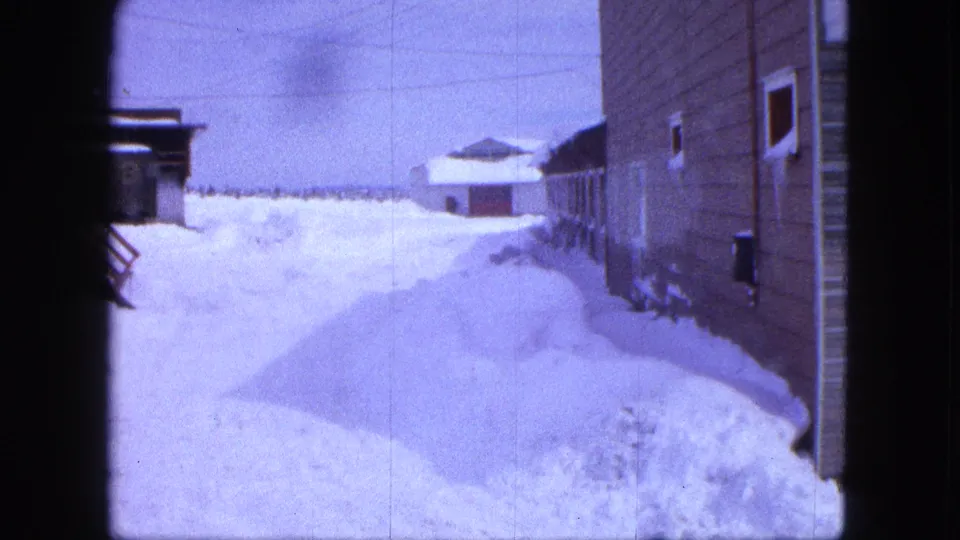 Handheld 8mm view of a deep snow-covered lane in Proctor, Minnesota, bordered by buildings and winter drifts.