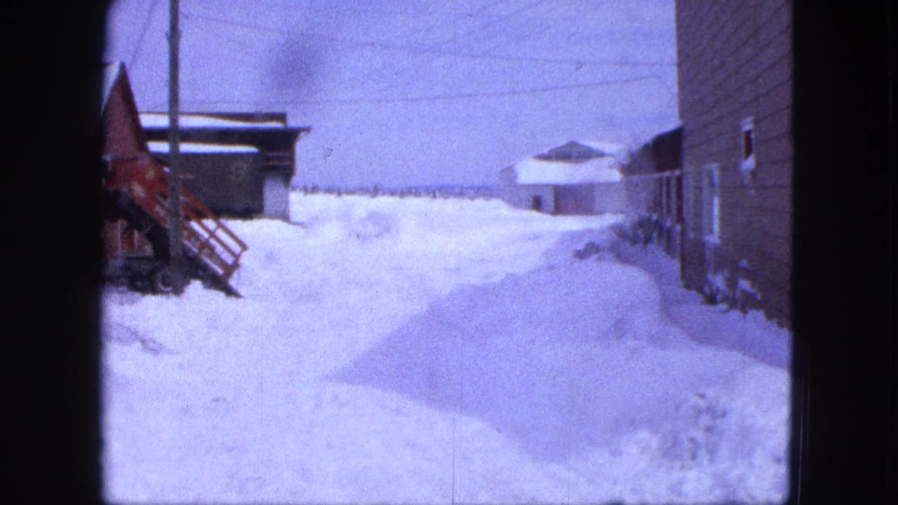 1963 Proctor, Minnesota frame with a snowbound farmyard, wooden buildings, utility lines, and a partly visible red tractor.