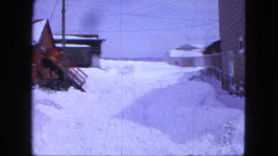 1963 Proctor, Minnesota home-movie frame showing a red tractor partly buried near a building amid deep snowdrifts.