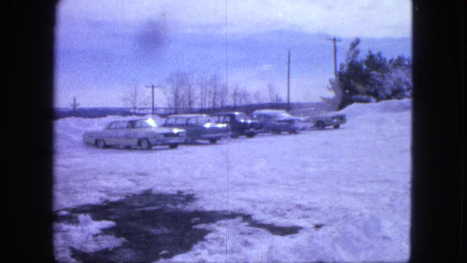 1963 Proctor, Minnesota frame showing several parked cars in a snow-covered rural lot with utility poles and winter trees behind them.
