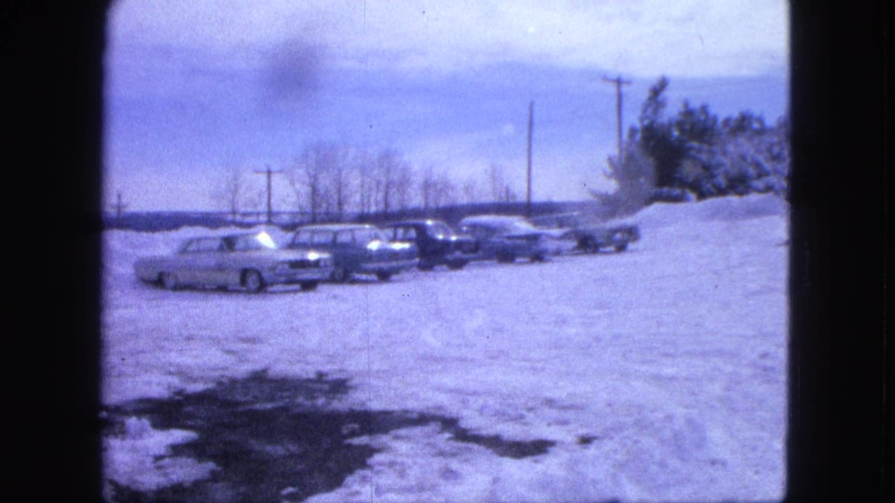 Parked cars lined up beside snowbanks under utility poles in a rural winter scene.