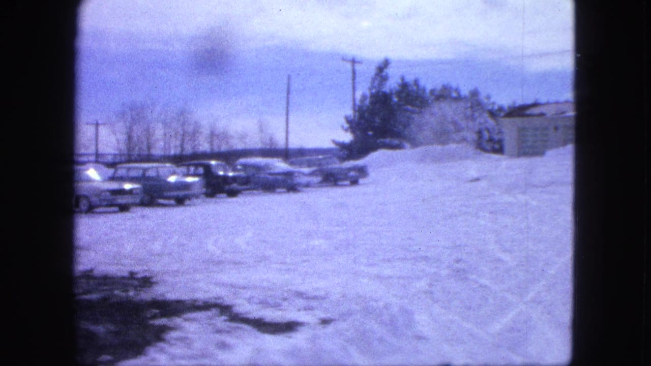 1963 Proctor, Minnesota frame with parked early 1960s cars partly framed by snowbanks, trees, utility poles, and a low building.