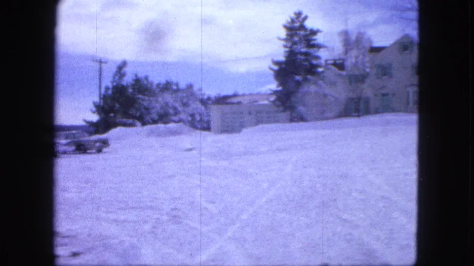 1963 Proctor, Minnesota frame showing snowy open ground, a partial car, trees, a small outbuilding, and a house at the right edge.