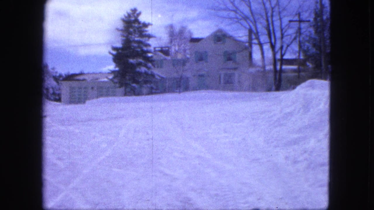 1963 Proctor, Minnesota 8mm frame with deep roadside snow, a large house, bare trees, utility poles, and a muted winter sky.