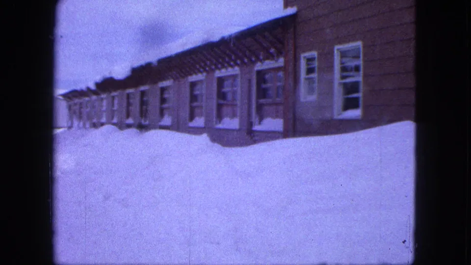 Handheld 8mm view of snowdrifts rising near windows on residential buildings in Proctor, Minnesota.