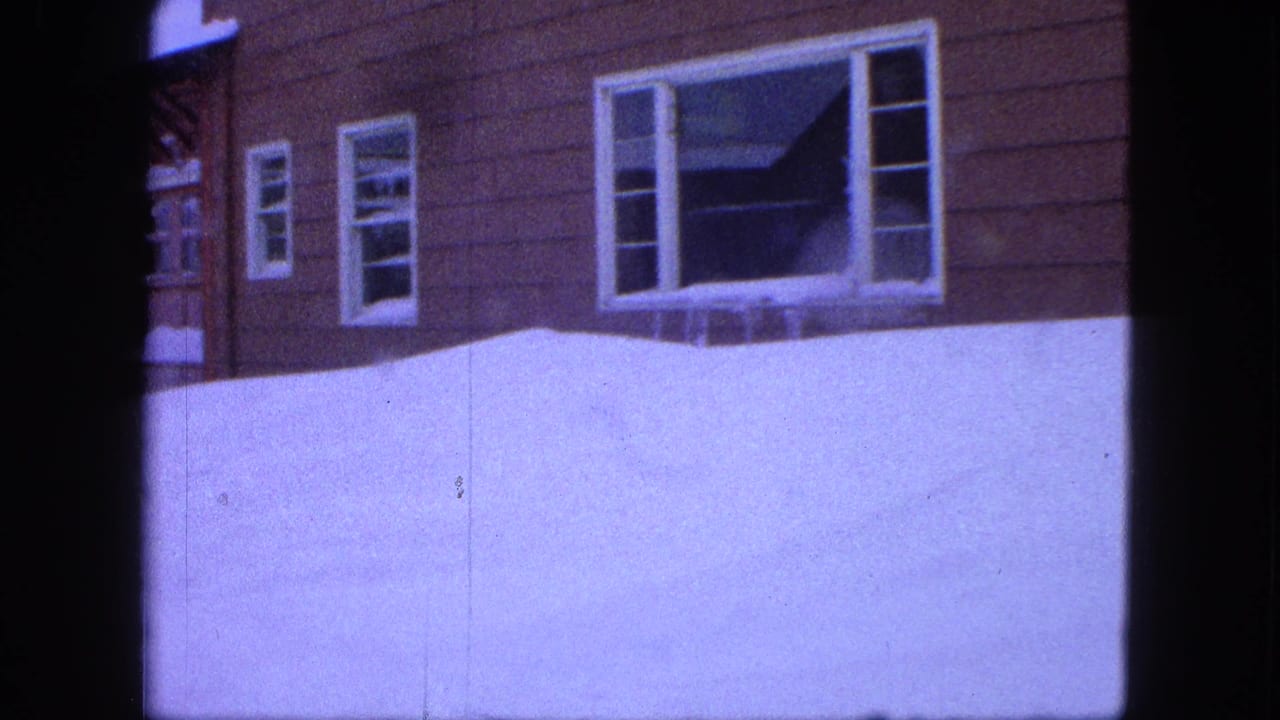 Snow-covered house wall with windows above a high drift.