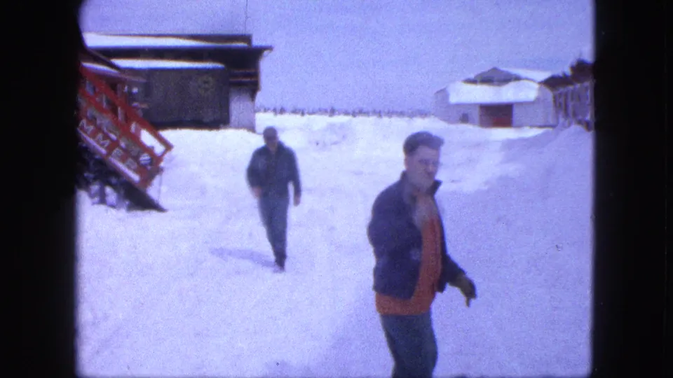 Two bundled men walk through deep snow outside a Proctor, Minnesota house in 1963 home-movie footage.