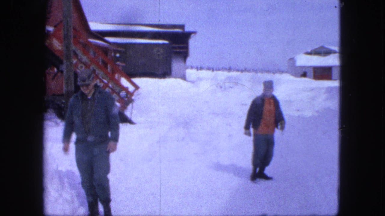 Two men are separated across a snowy yard in Proctor, Minnesota, with a red structure, snowbanks, and a small building visible behind them.