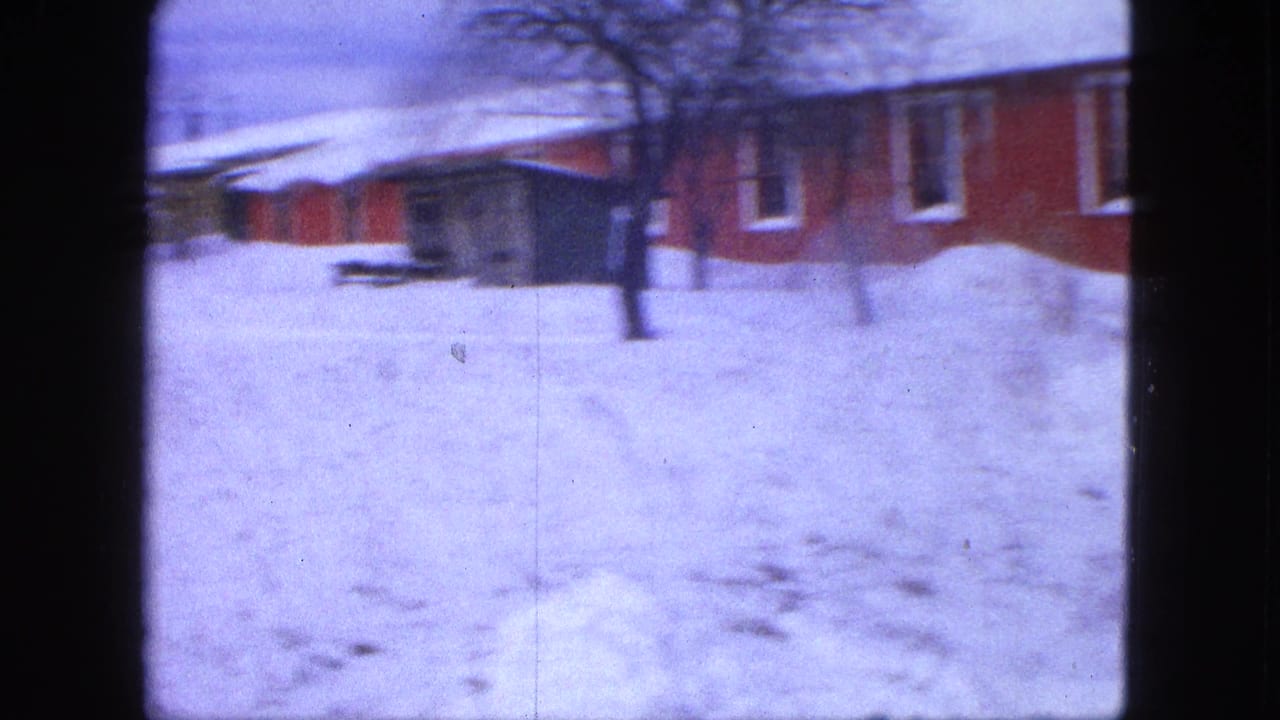 1963 Proctor, Minnesota home-movie frame showing a snowy yard, a red building, bare tree, and heavy snow cover.
