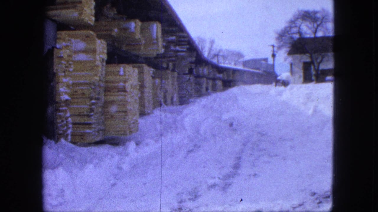 Proctor, Minnesota winter yard view with lumber stacks along a shed and snowdrifts filling the foreground.