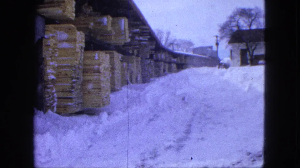 Proctor, Minnesota winter yard view with lumber stacks along a shed and snowdrifts filling the foreground.