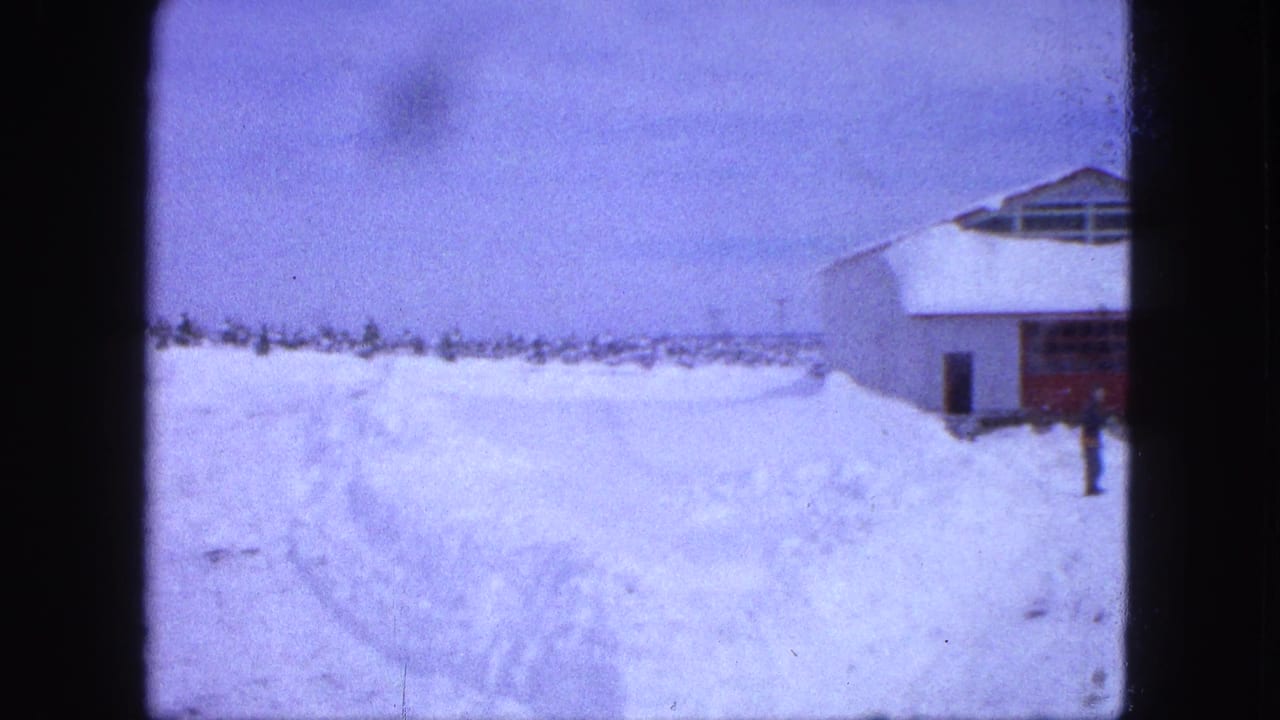 A bundled person walks through deep snow toward a white building with a red door.