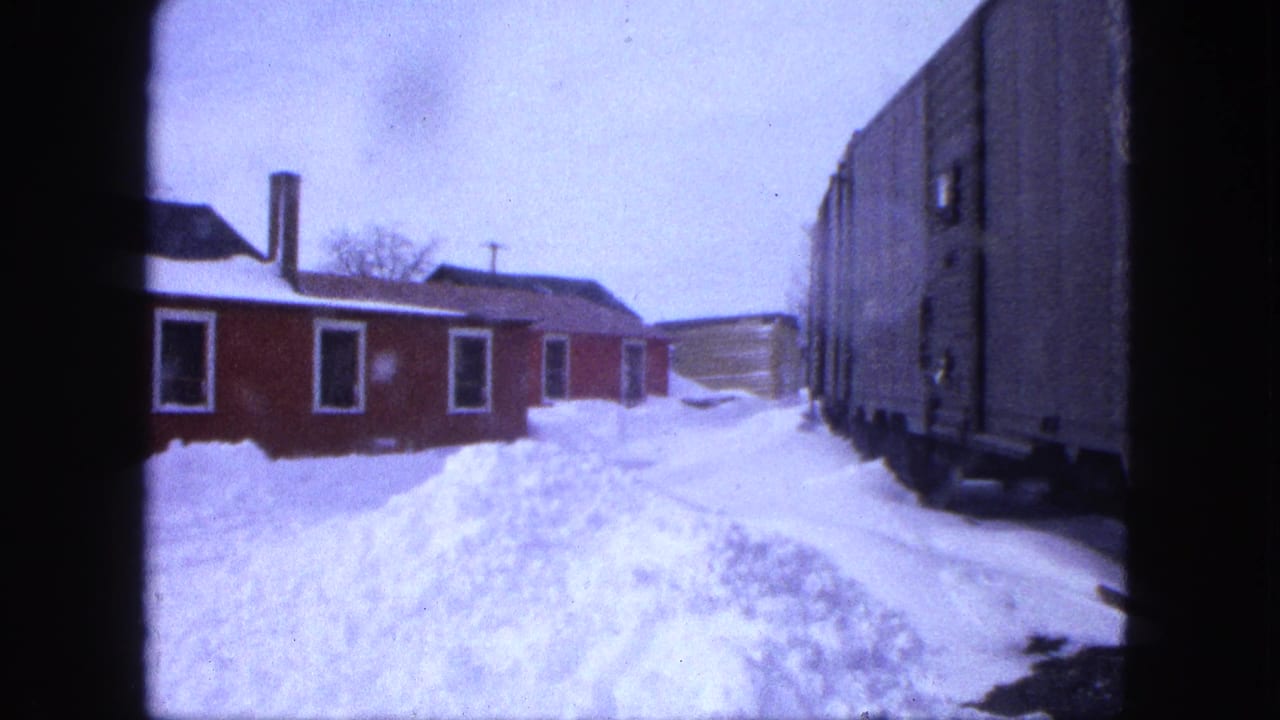 1963 Proctor, Minnesota view of a red work building, snow piled high, and a freight car along the right side.
