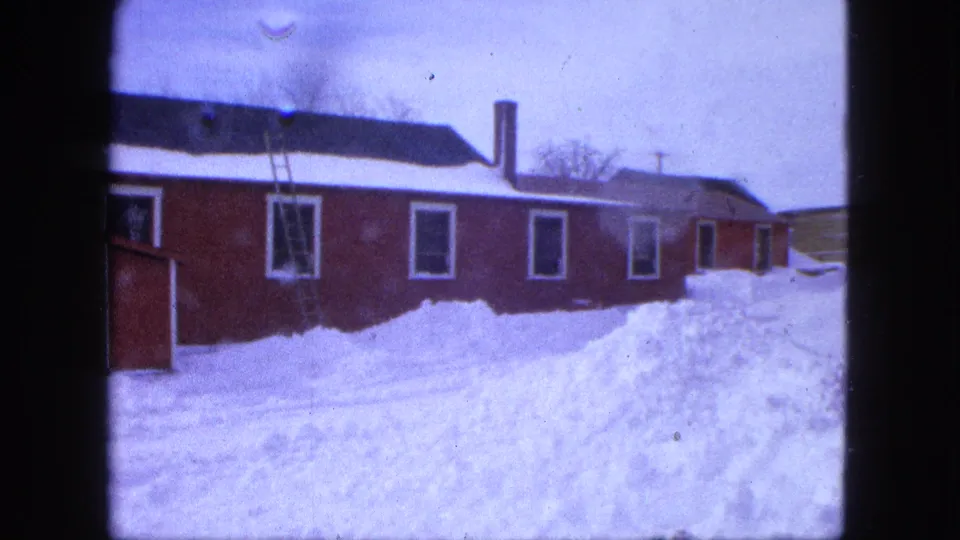 1963 Proctor, Minnesota 8mm frame showing a red house, deep snow, white-trimmed windows, and a ladder leaning near the wall.