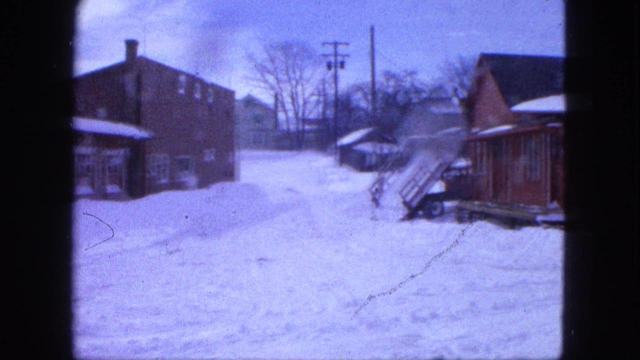 Snow-covered town street with brick buildings, bare trees, and utility poles.