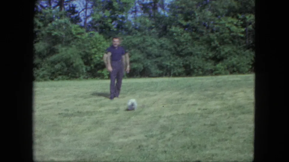 In 1963 Saint Paul home-movie footage, a man stands on a grassy backyard lawn as a small white dog waits nearby.