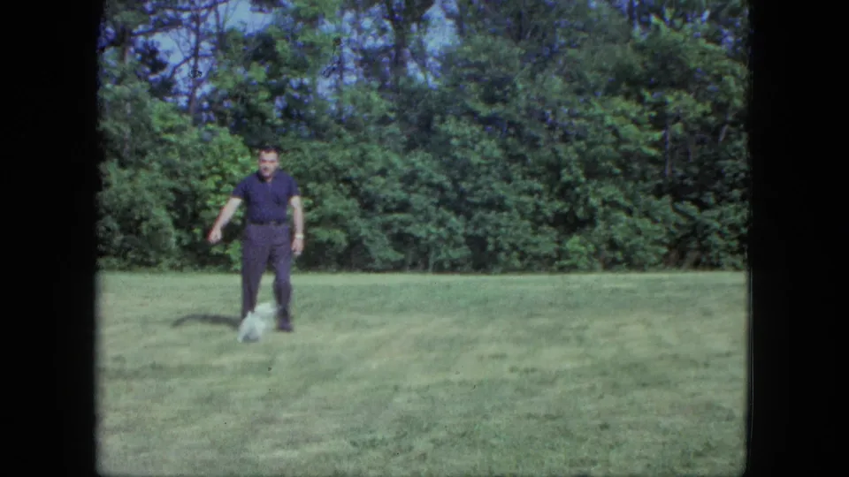 The small white dog returns near the man on the open lawn, captured in 1963 8mm home-movie footage from Saint Paul.