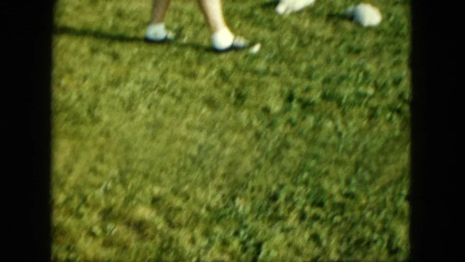 1963 Saint Paul home-movie frame showing a grassy backyard with only a person's lower legs and white shoes partly in view.
