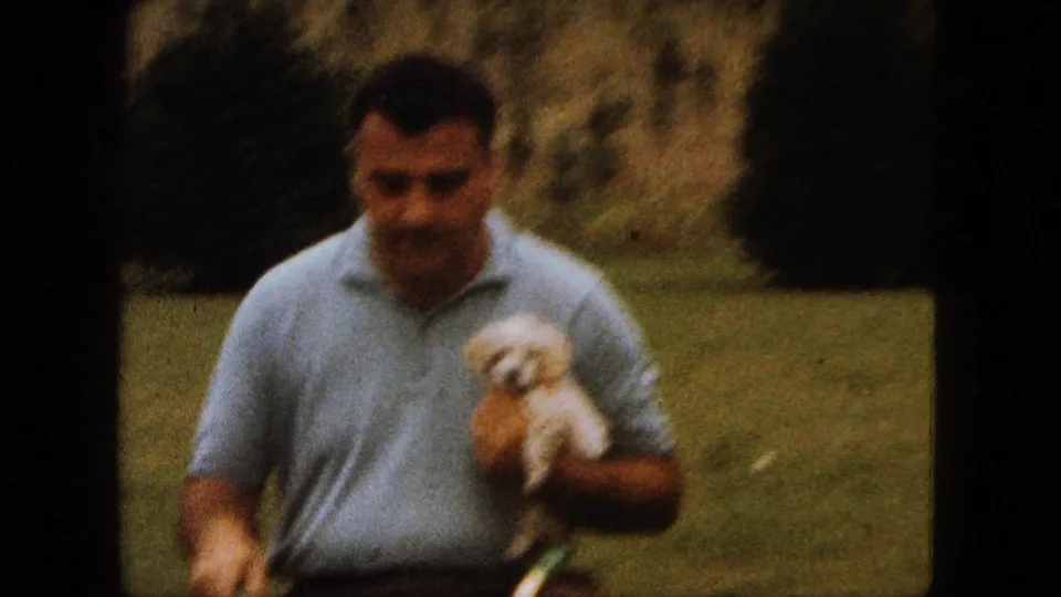In the grassy yard, the man rides with the small white poodle puppy held in one arm, framed in soft 8mm focus.