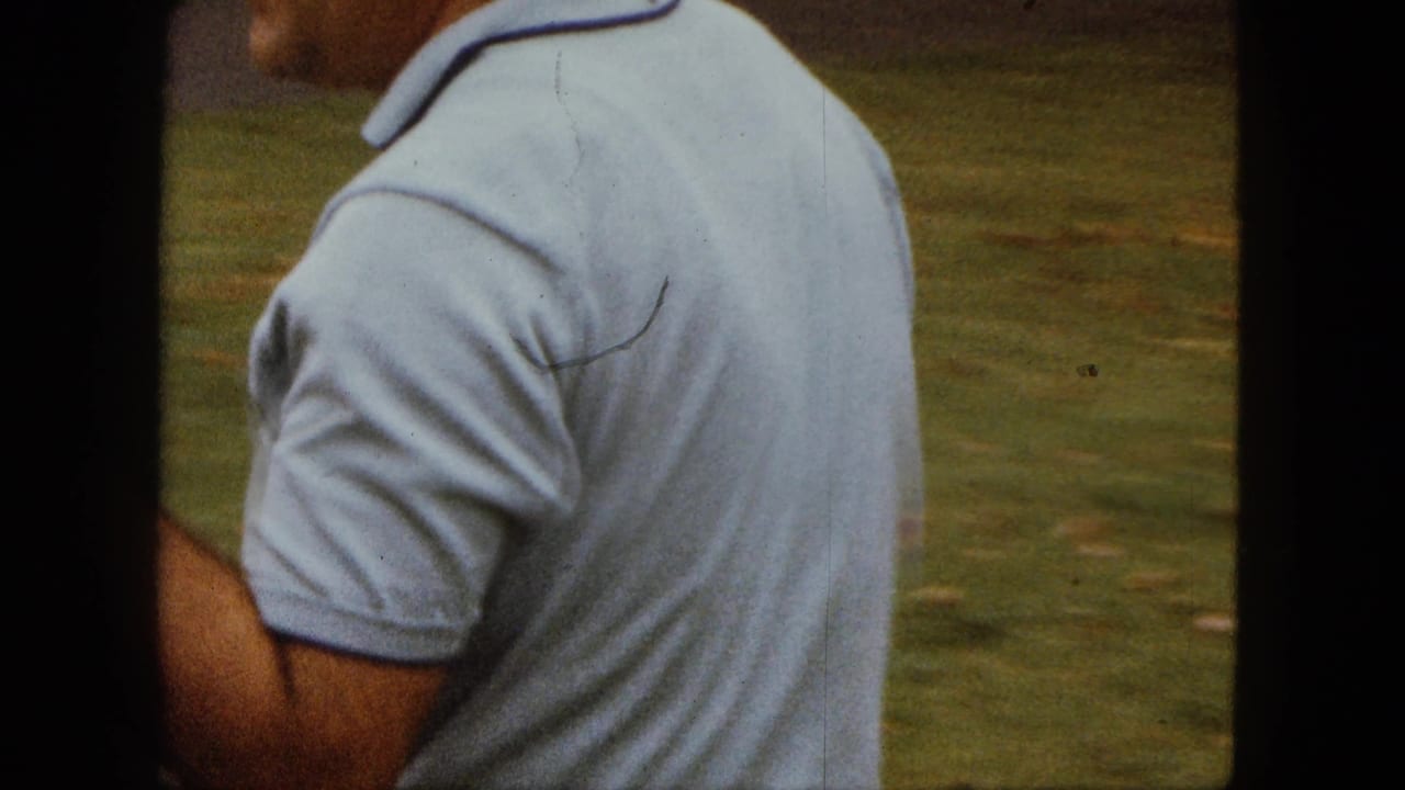 The man turns away from the camera in a Saint Paul yard, still holding the small white dog against his shirt.