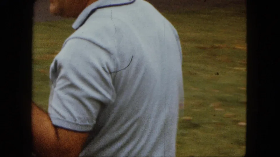 The man turns away from the camera in a Saint Paul yard, still holding the small white dog against his shirt.