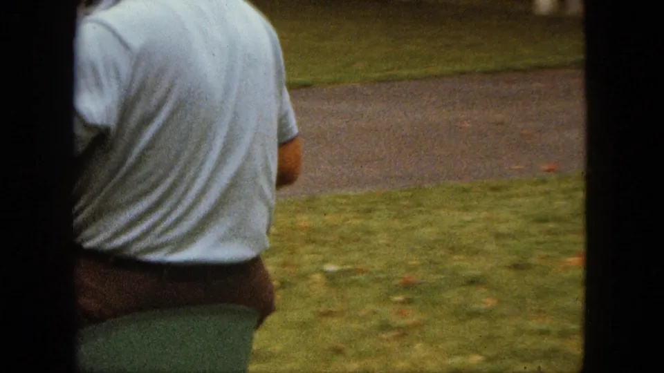 The man walks across the yard near a vintage green and white child's ride-on toy in 1963 Saint Paul footage.