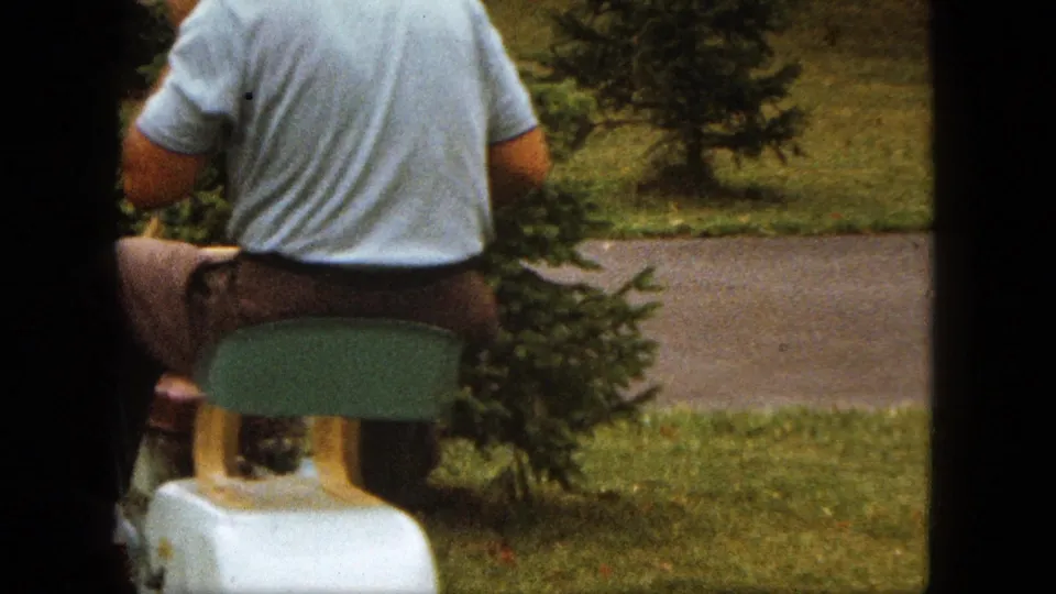 A man in a light blue polo moves past an evergreen shrub and child's ride-on toy in a Saint Paul yard.