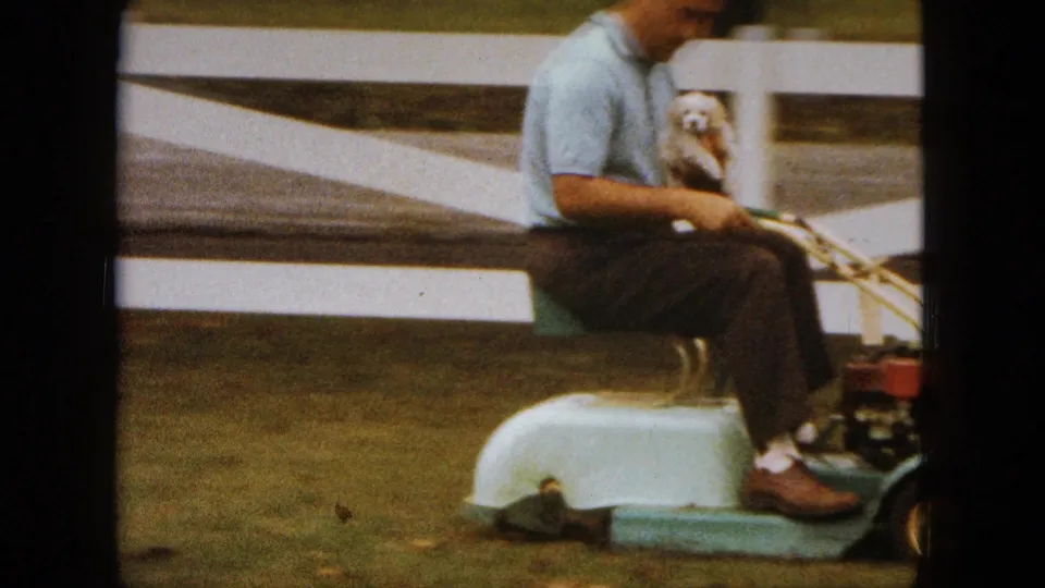 A side view shows the man on the vintage mower with the puppy in his lap, near the white fence in Saint Paul.