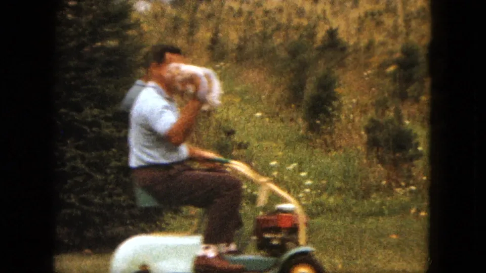 A soft 8mm frame shows the man riding near shrubs and tall grass while holding the puppy close to his face.