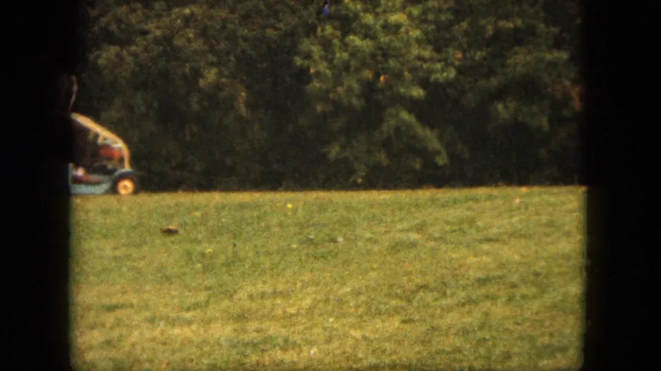 A man on a small riding mower continues across a green Saint Paul backyard in this 1963 8mm home-movie frame.