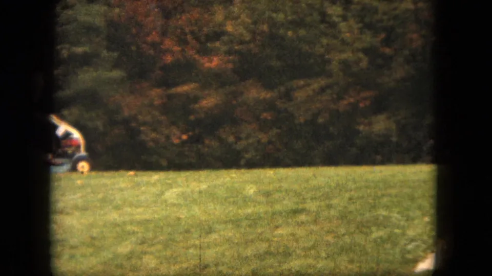 A vintage riding mower appears on a Saint Paul backyard lawn, with dense trees and early autumn color behind it.