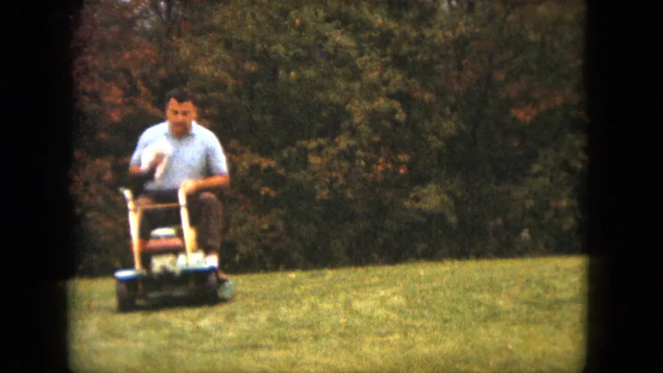 The mower turns toward the camera as the man holds the dog on the grassy Saint Paul yard in soft 8mm color.