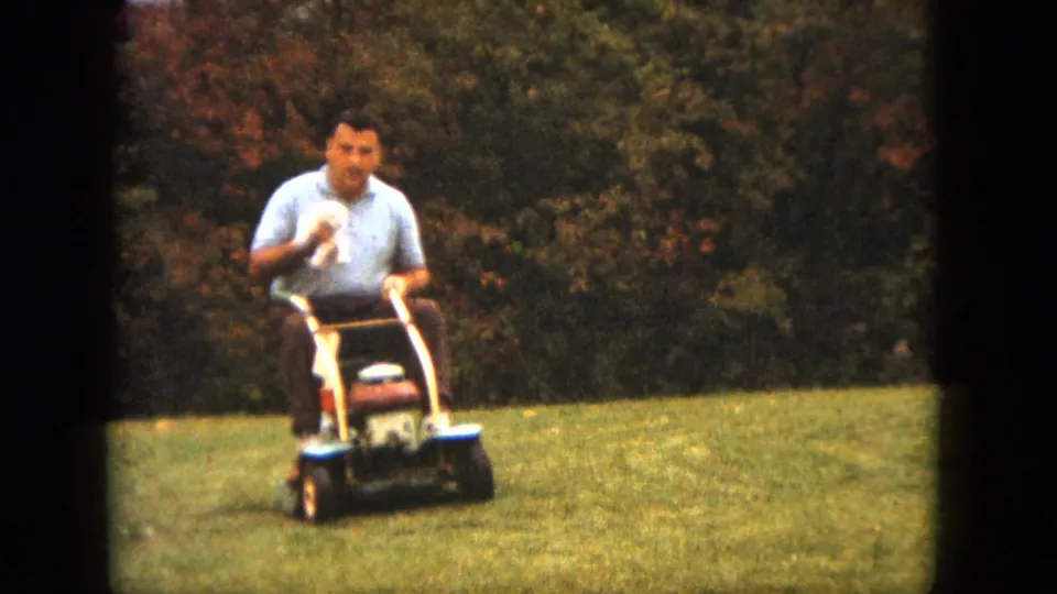 At the end of the 1963 Saint Paul clip, the man glances toward the camera while riding the mower with the dog.
