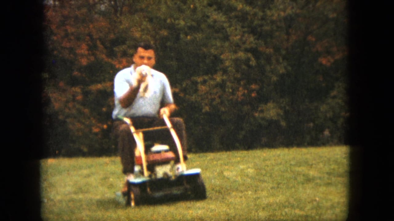 In 1963 Saint Paul home-movie footage, a man on a ride-on mower holds a small white puppy while crossing a grassy yard.