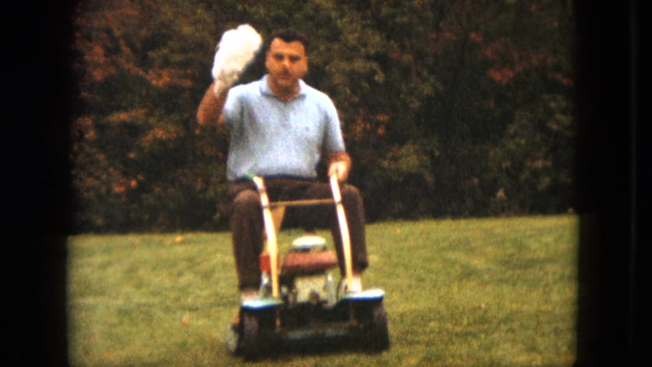 The man rides a vintage mower in a Saint Paul yard and lifts the white puppy toward the camera.