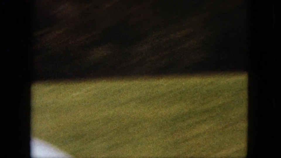A soft, partially obscured 8mm frame shows green lawn and dark frame edges during the camera movement.