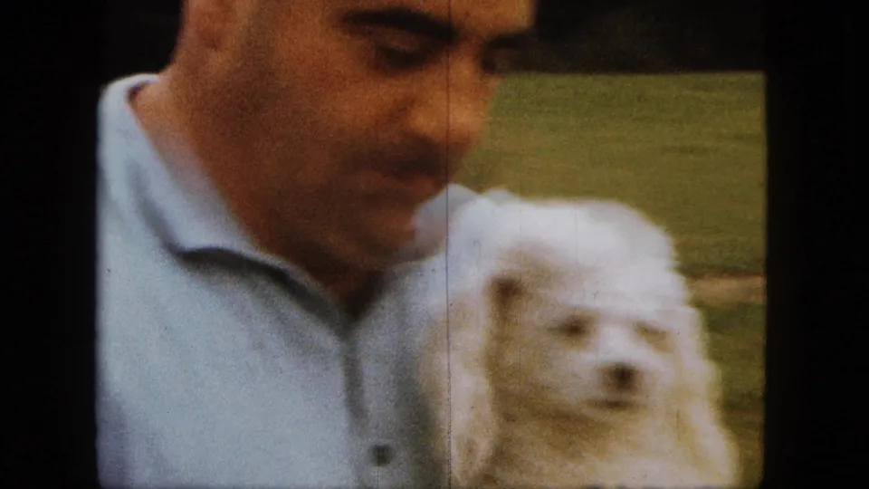 Soft-focus 8mm frame of a man and white poodle close to the camera in a 1963 Saint Paul backyard.