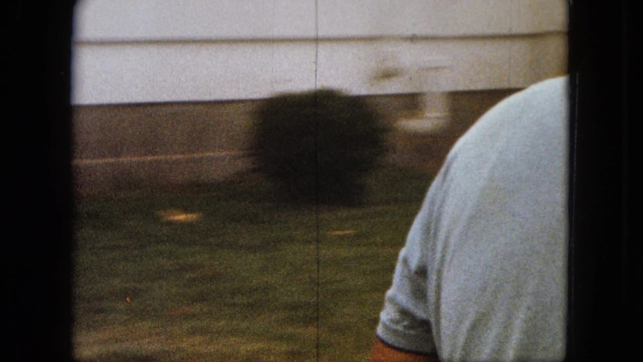 Man in a light shirt partly visible beside a lawn and pale building surface.