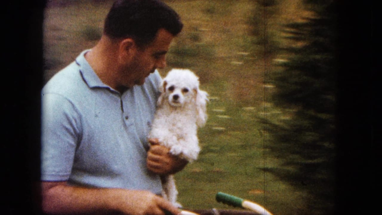 1963 Saint Paul 8mm frame showing a man holding a small white poodle as bicycle handlebars pass through the lower foreground.